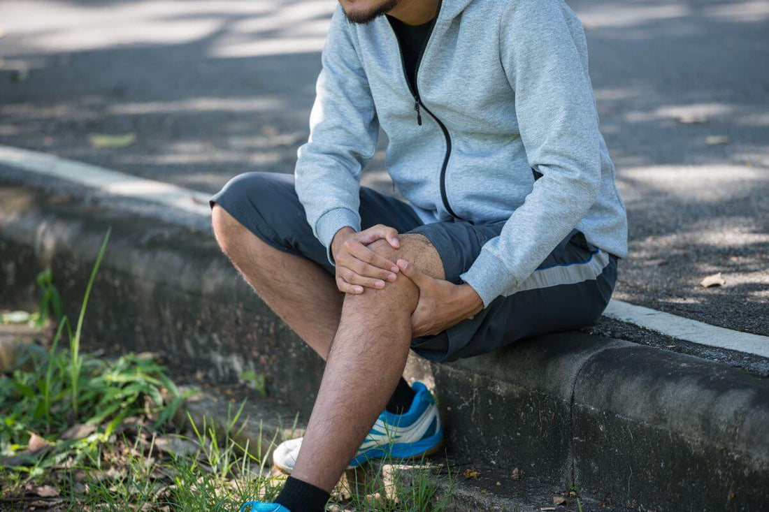 Man sitting outdoors and holding his knee due to muscle pain after physical activity