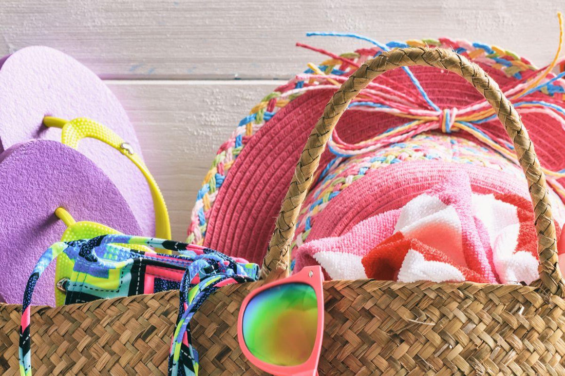 Woven beach bag packed with towels, flip-flops, a sun hat, swimwear, and sunglasses for a summer trip