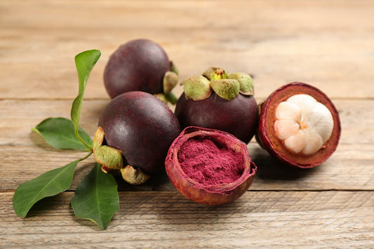 Fresh whole and cut mangosteen fruits displayed on a wooden surface