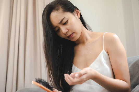 Woman checking her hair and scalp while holding a hairbrush, showing concern about dryness or sensitivity