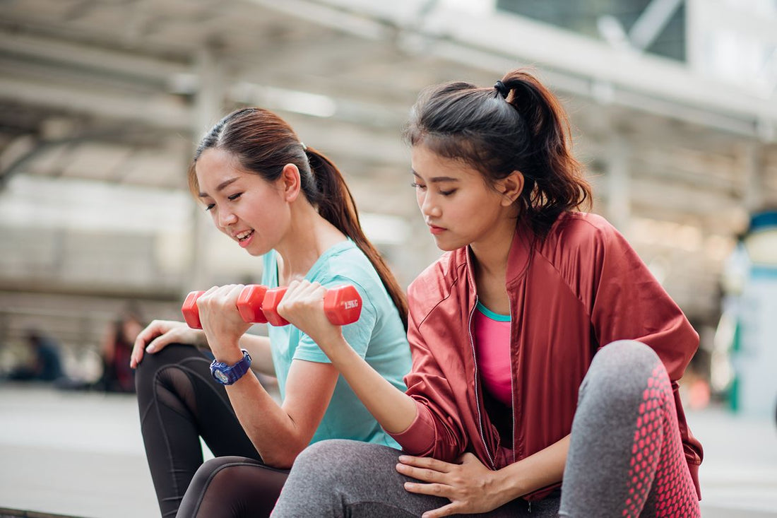 Two women resting after exercise, with one holding a dumbbell and the other supporting her arm