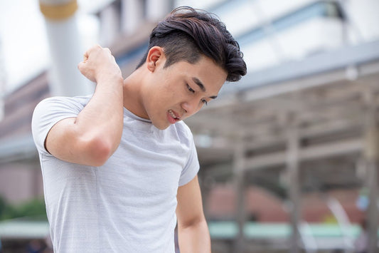 Man standing outdoors while holding the back of his neck due to muscle discomfort after a physically demanding day